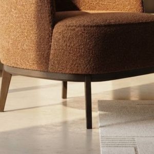 Détail du tissu bouclé terracotta et du pied en bois du fauteuil Megan
